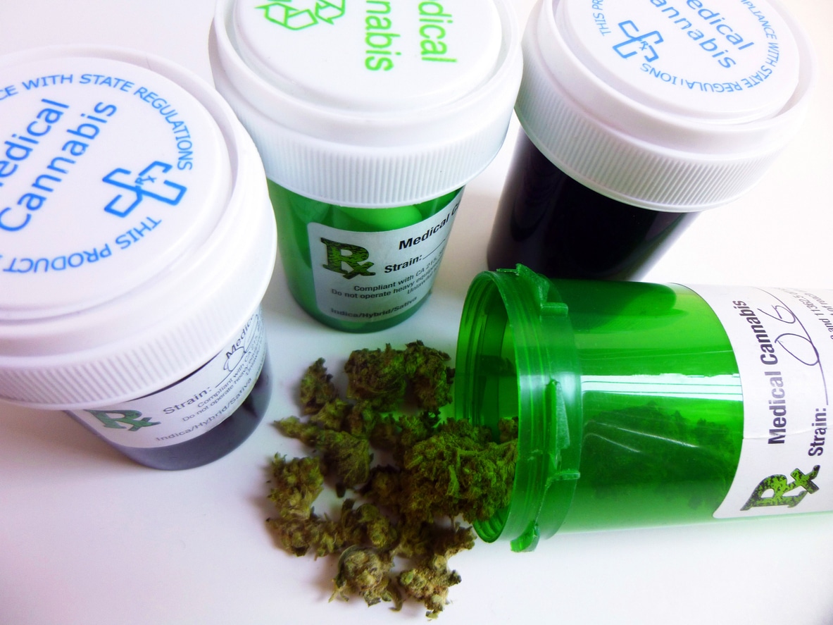 Four medical marijuana prescription bottles close together with one open and spilling out cannabis buds.