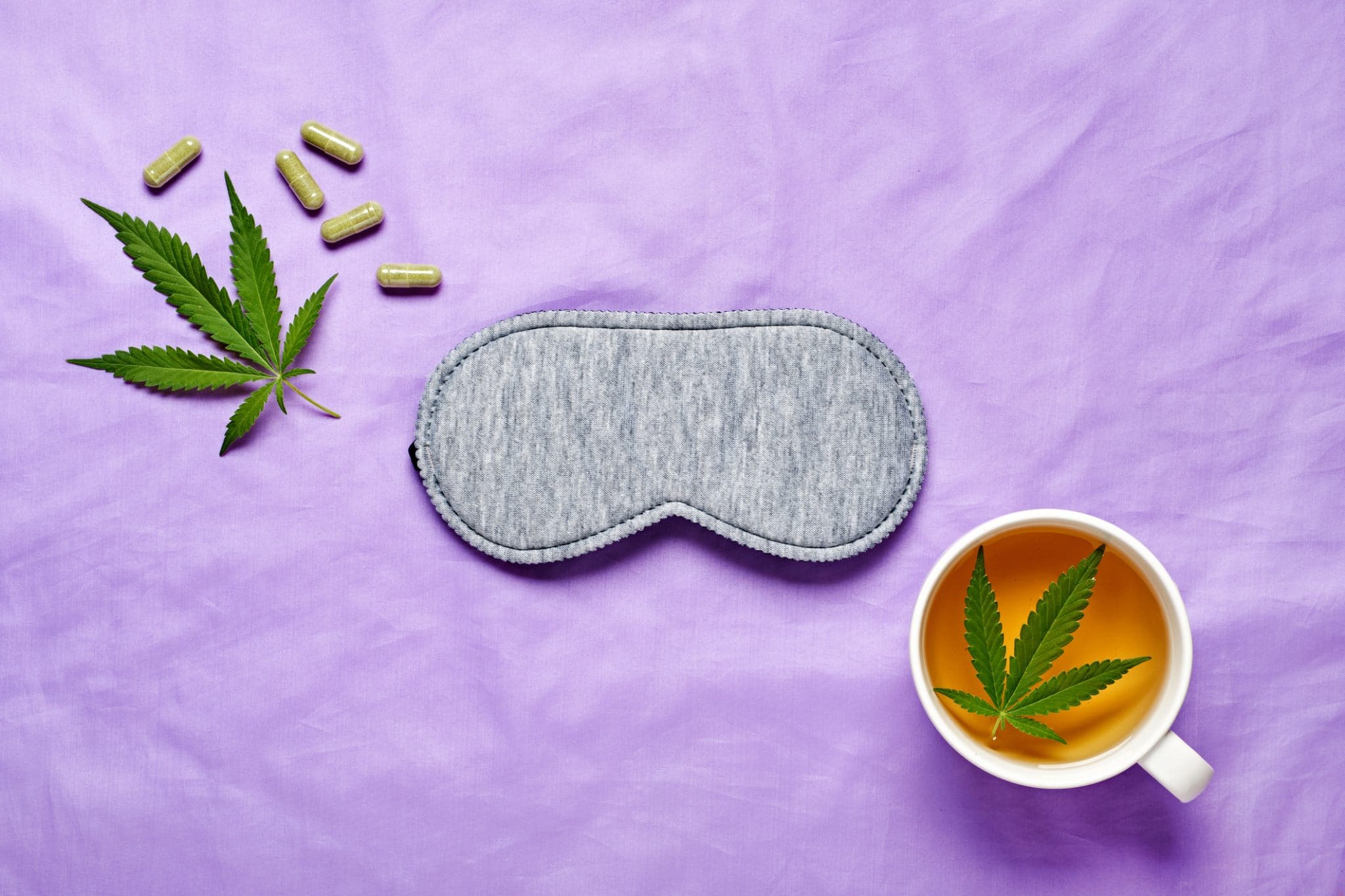 A cannabis leaf, sleep mask, and cannabis tea set against a light purple background signifying the link between cannabis and sleep.